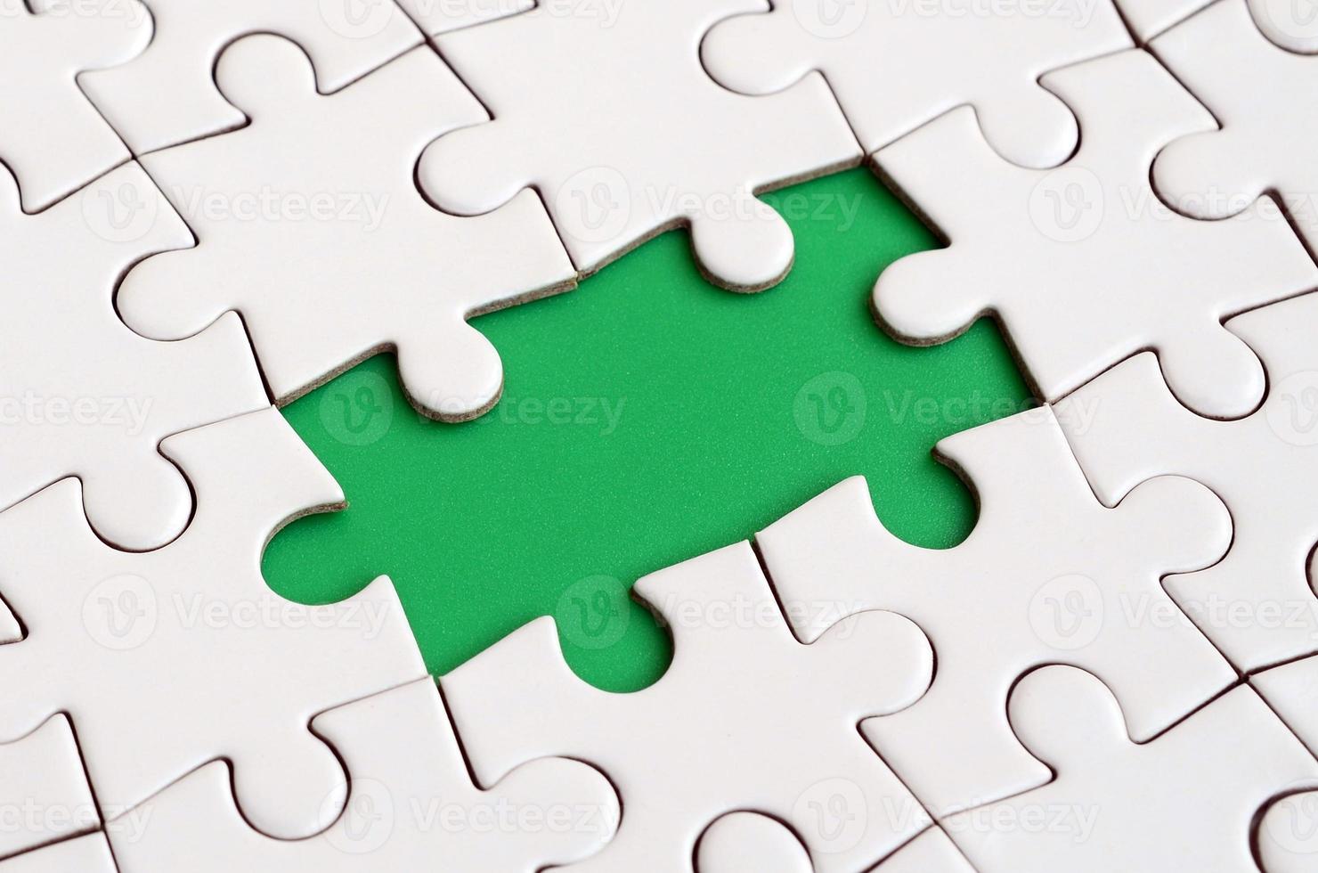 Close-up texture of a white jigsaw puzzle in assembled state with missing elements forming a green pad for text. Copy space photo