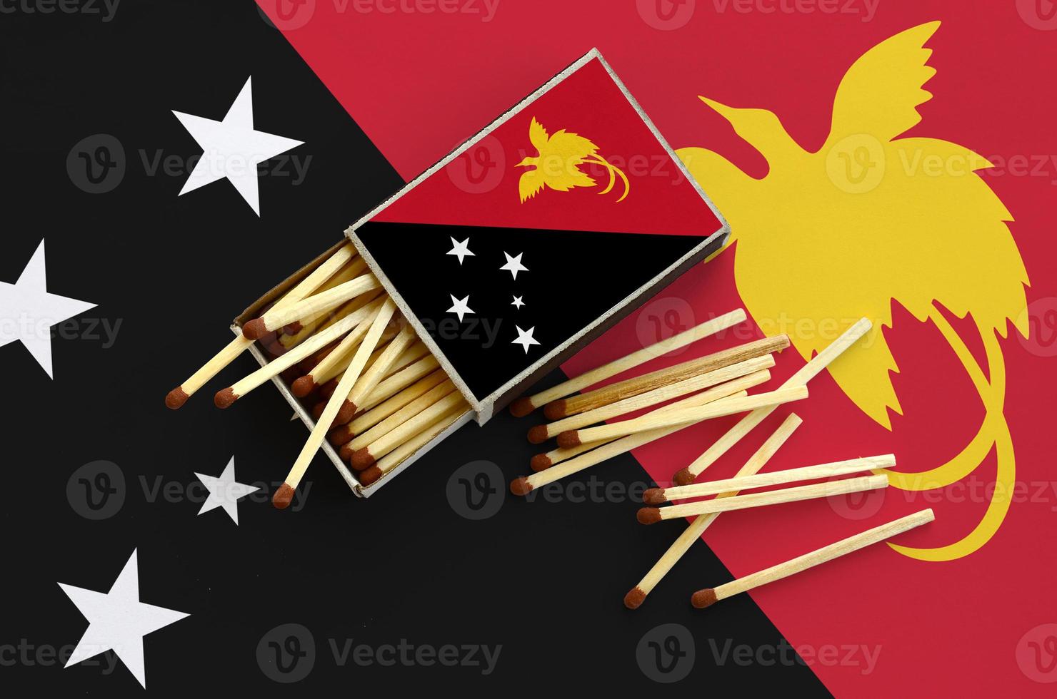 Papua New Guinea flag is shown on an open matchbox, from which several matches fall and lies on a large flag photo