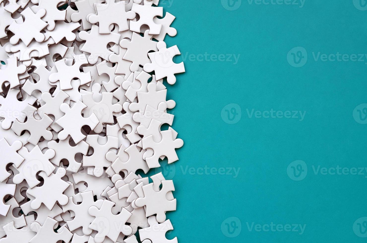 A pile of uncombed elements of a white jigsaw puzzle lies on the background of a blue surface. Texture photo with copy space for text