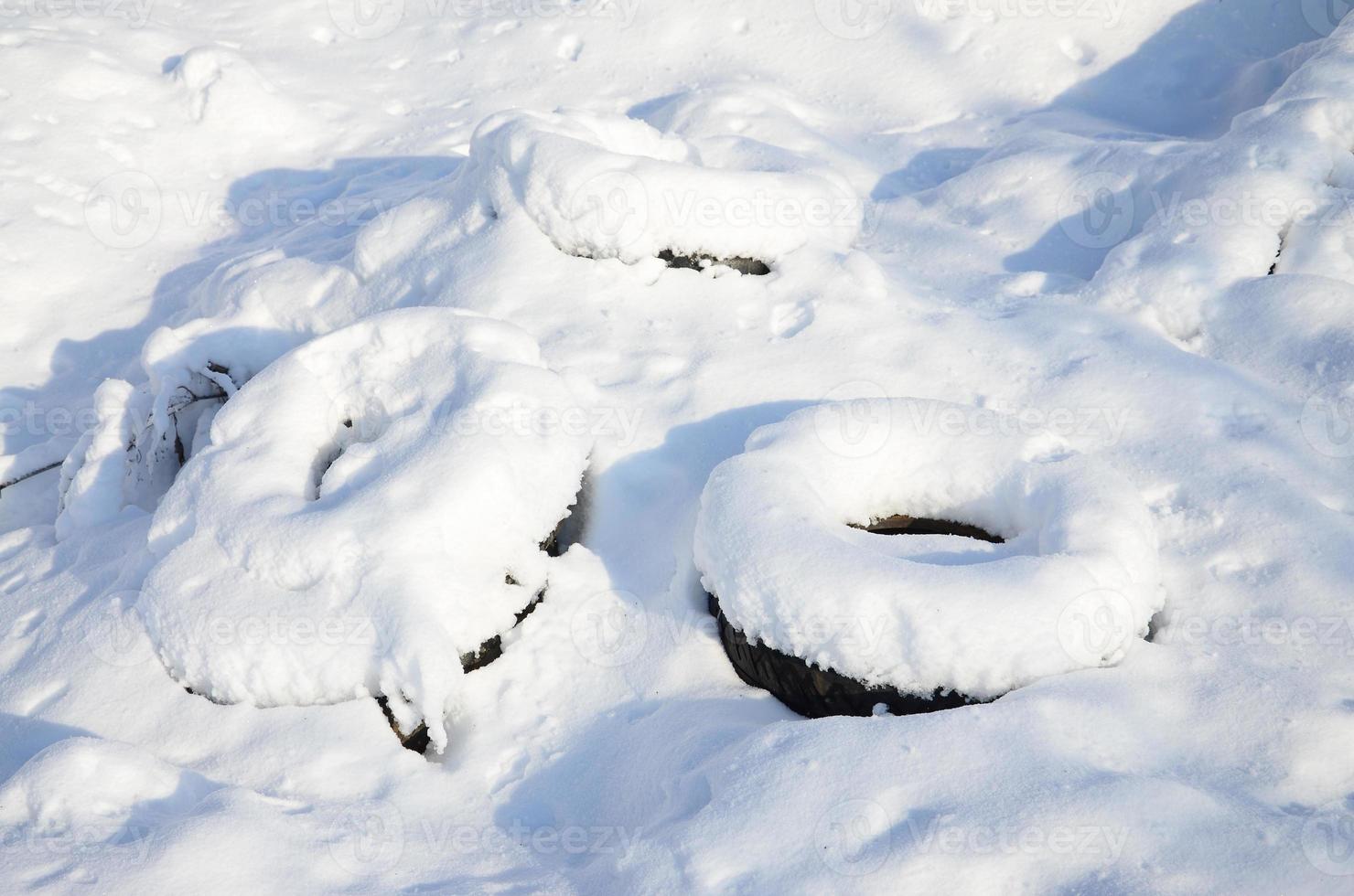 Used and discarded car tires lie on the side of the road, covered with a thick layer of snow photo