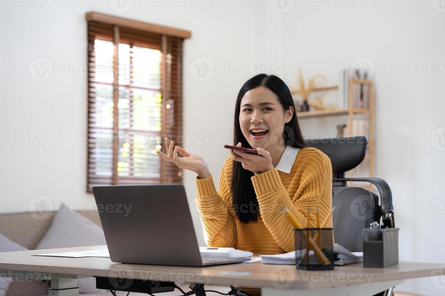 hermosa y sonriente mujer de negocios asiática analizando gráficos y gráficos que muestran los cambios en el mercado y sosteniendo el teléfono inteligente en casa foto