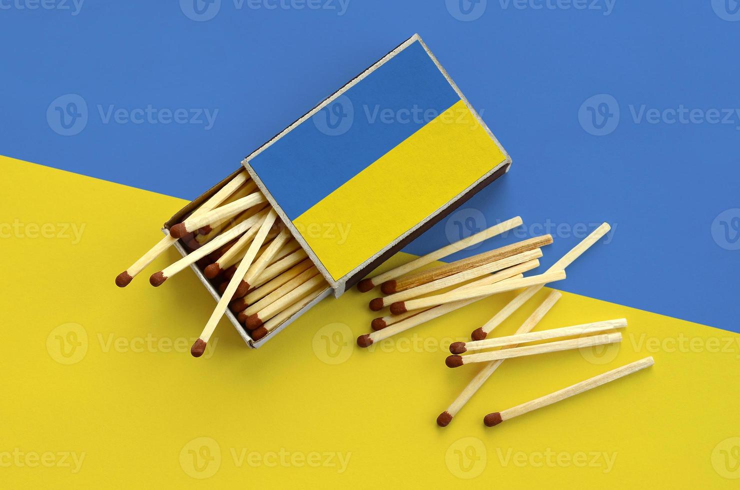 Ukraine flag is shown on an open matchbox, from which several matches fall and lies on a large flag photo