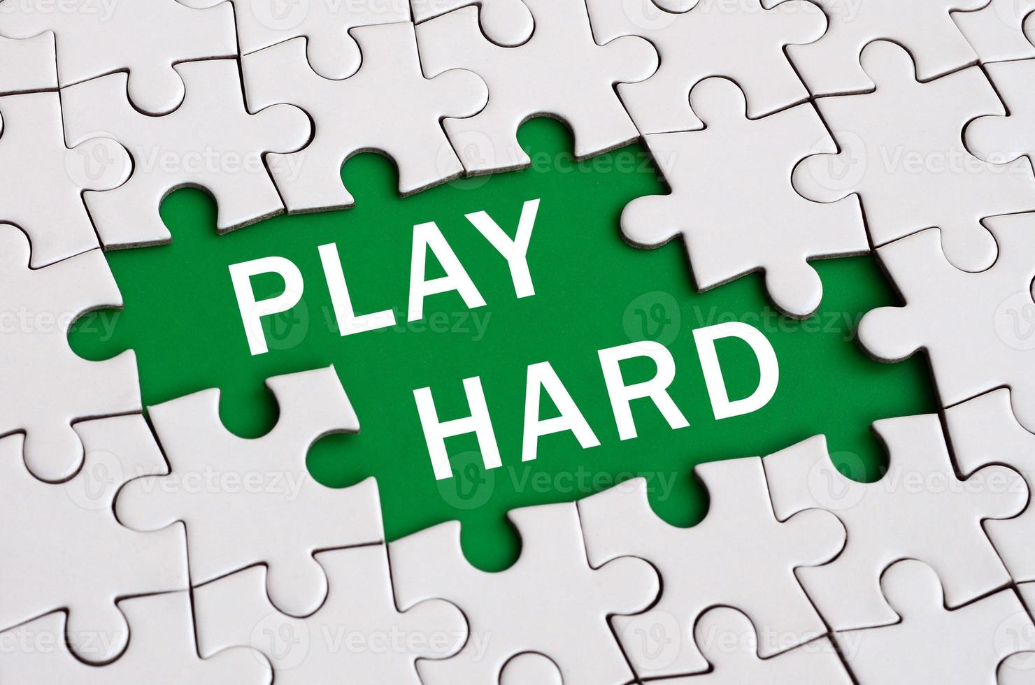 White jigsaw puzzle in assembled state with missing elements forming a green space with white inscription. Play hard photo