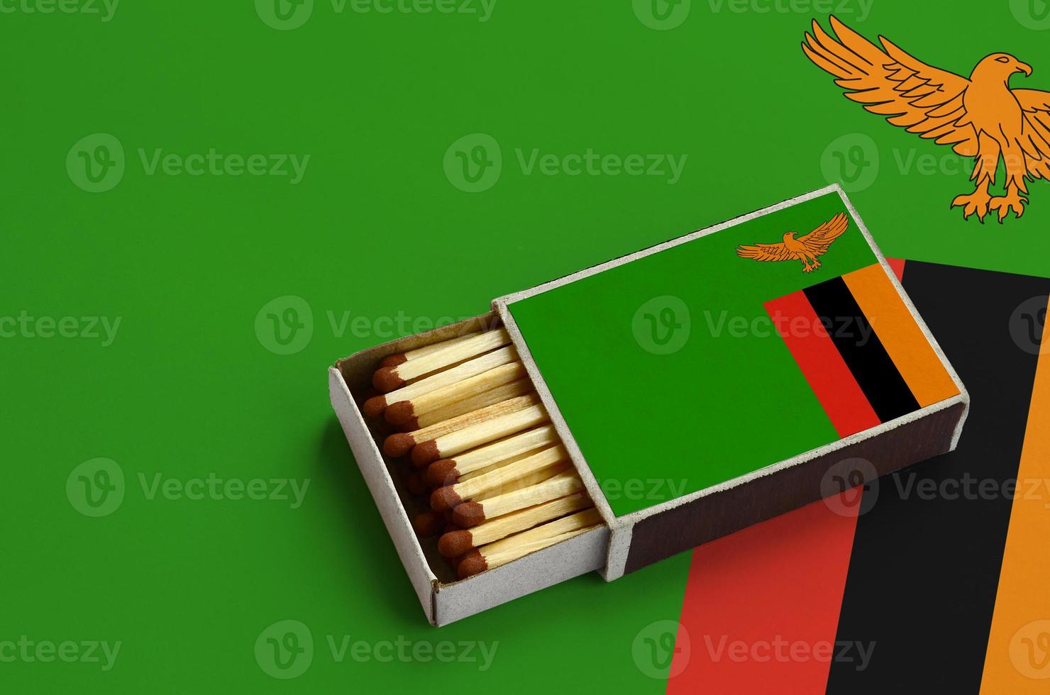 Zambia flag is shown in an open matchbox, which is filled with matches and lies on a large flag photo