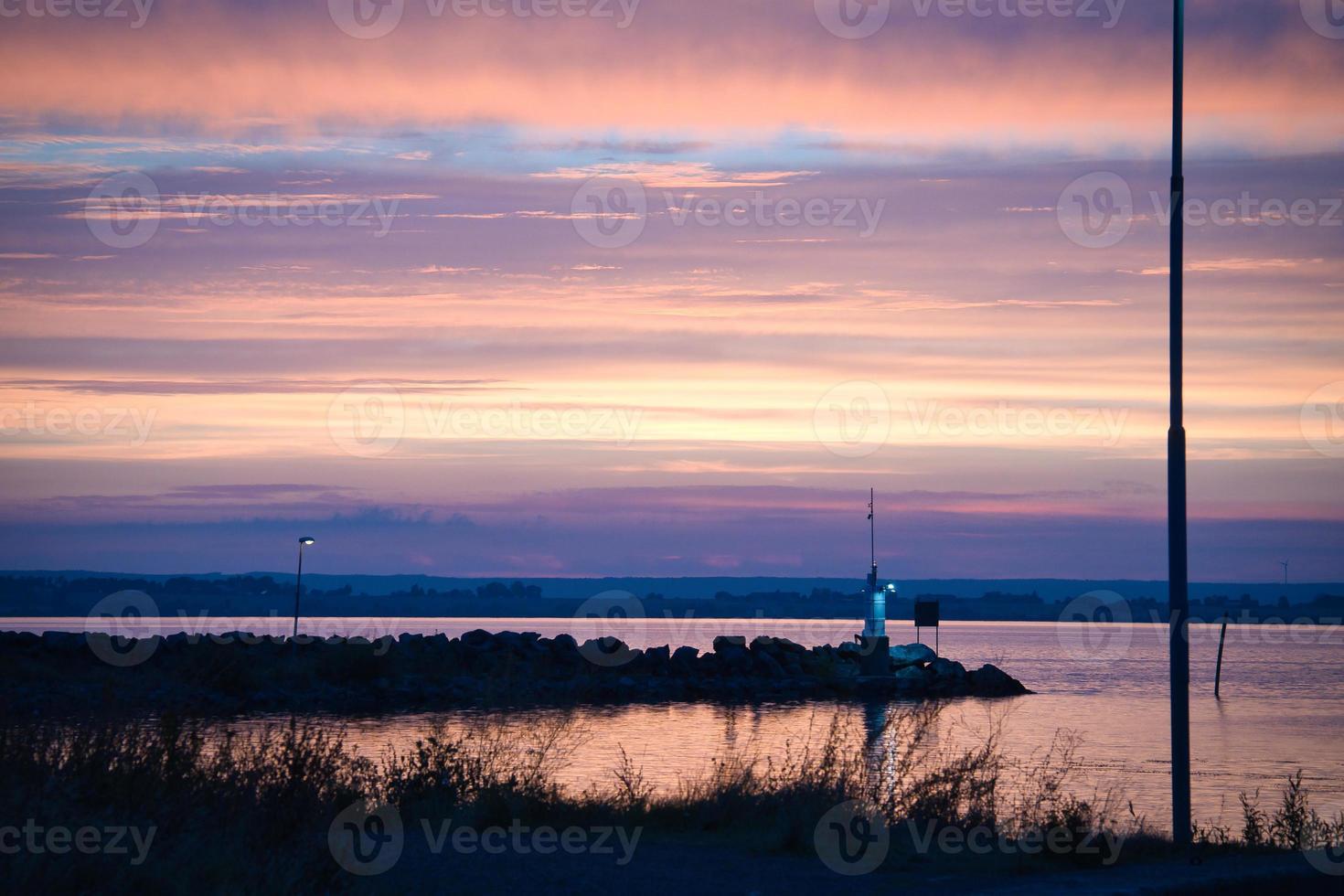 puesta de sol en suecia en el puerto del lago vaetten. faro en el fondo foto