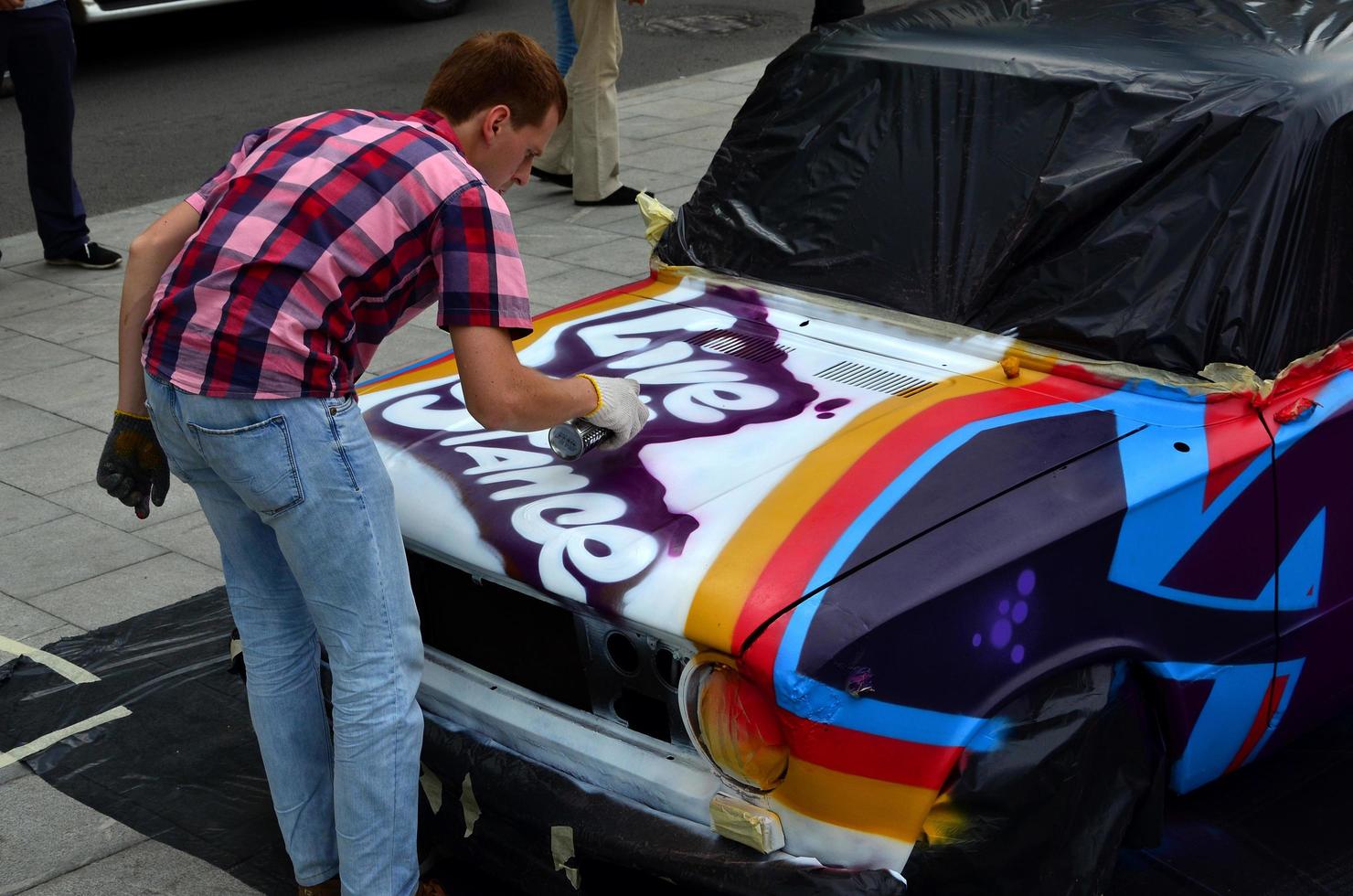 KHARKOV, UKRAINE - MAY 27, 2017 Festival of street art. Young guys draw graffiti on the car body in the city center. The process of drawing color graffiti on a car with aerosol cans photo