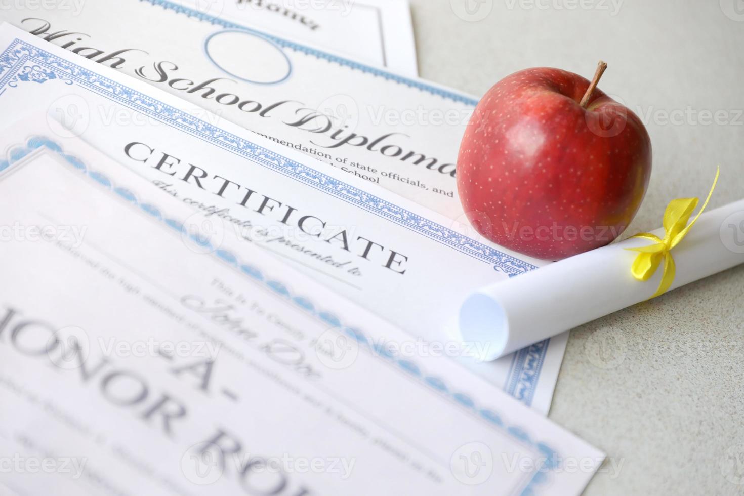 A honor roll recognition, certificate of achievement and high school diploma lies on table with small scroll and red apple. Education documents photo
