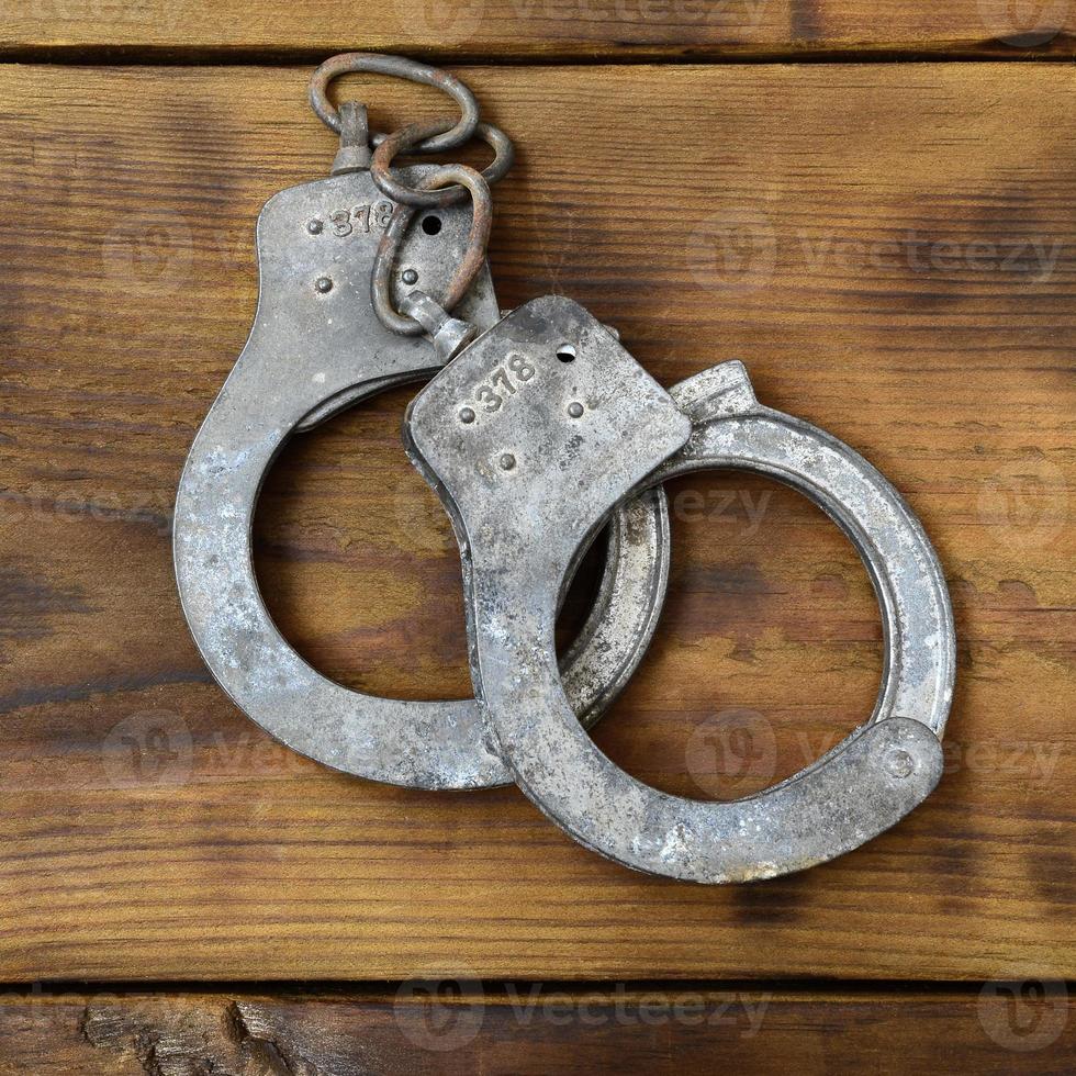 Old and rusty police handcuffs lie on a scratched wooden surface. The concept of an old crime photo