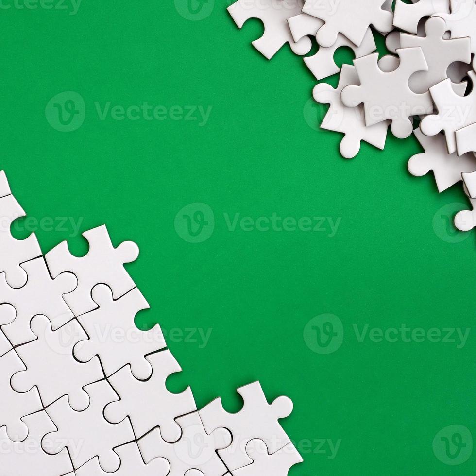 Fragment of a folded white jigsaw puzzle and a pile of uncombed puzzle elements against the background of a green surface. Texture photo with space for text