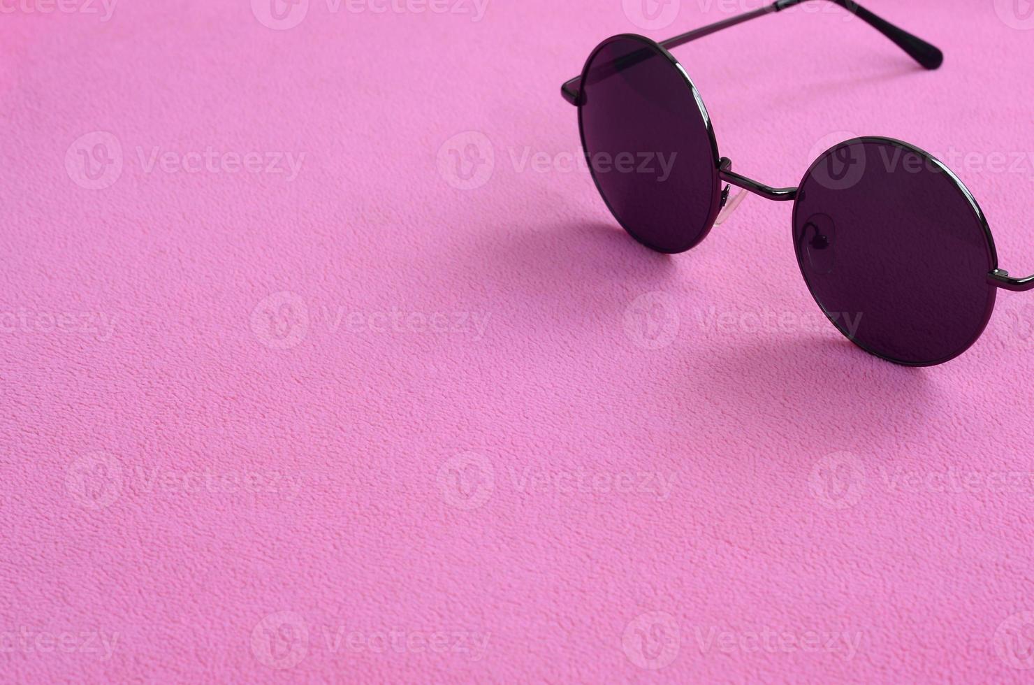 Stylish black sunglasses with round glasses lies on a blanket made of soft and fluffy light pink fleece fabric. Fashionable background picture in female colors photo