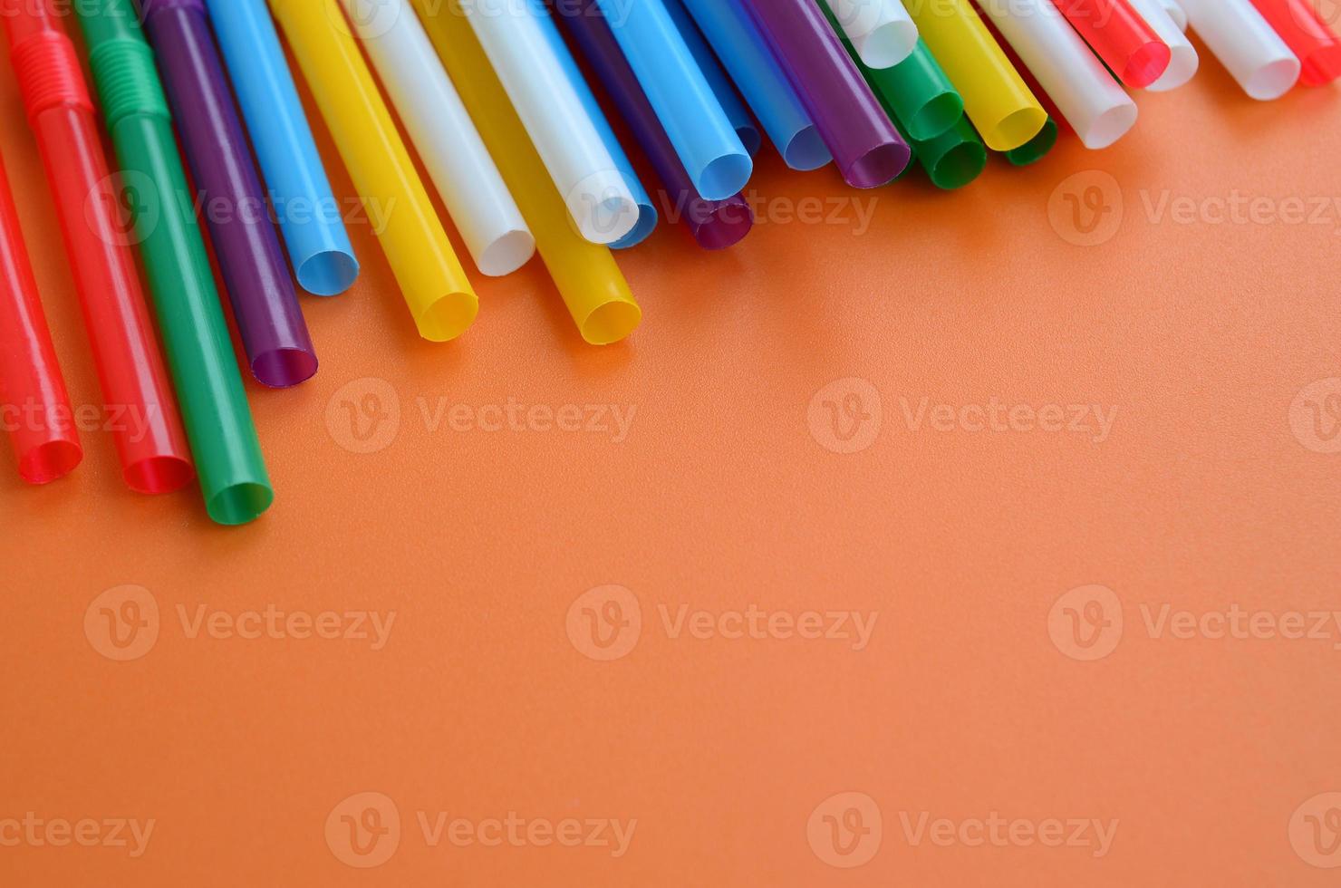 Many colorful straws for drinks lies on a bright orange background surface photo