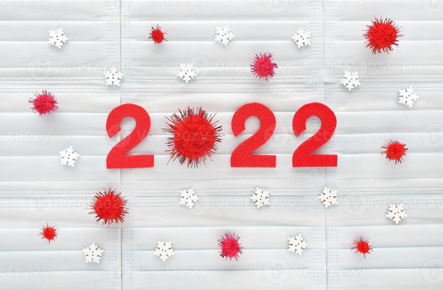 Red numbers 2022 of the year cut out of red felt on light blue medical masks background with wooden white snowflakes and red pompons. Zero is fluffy pom pom. Review of the coved-19 year results. photo