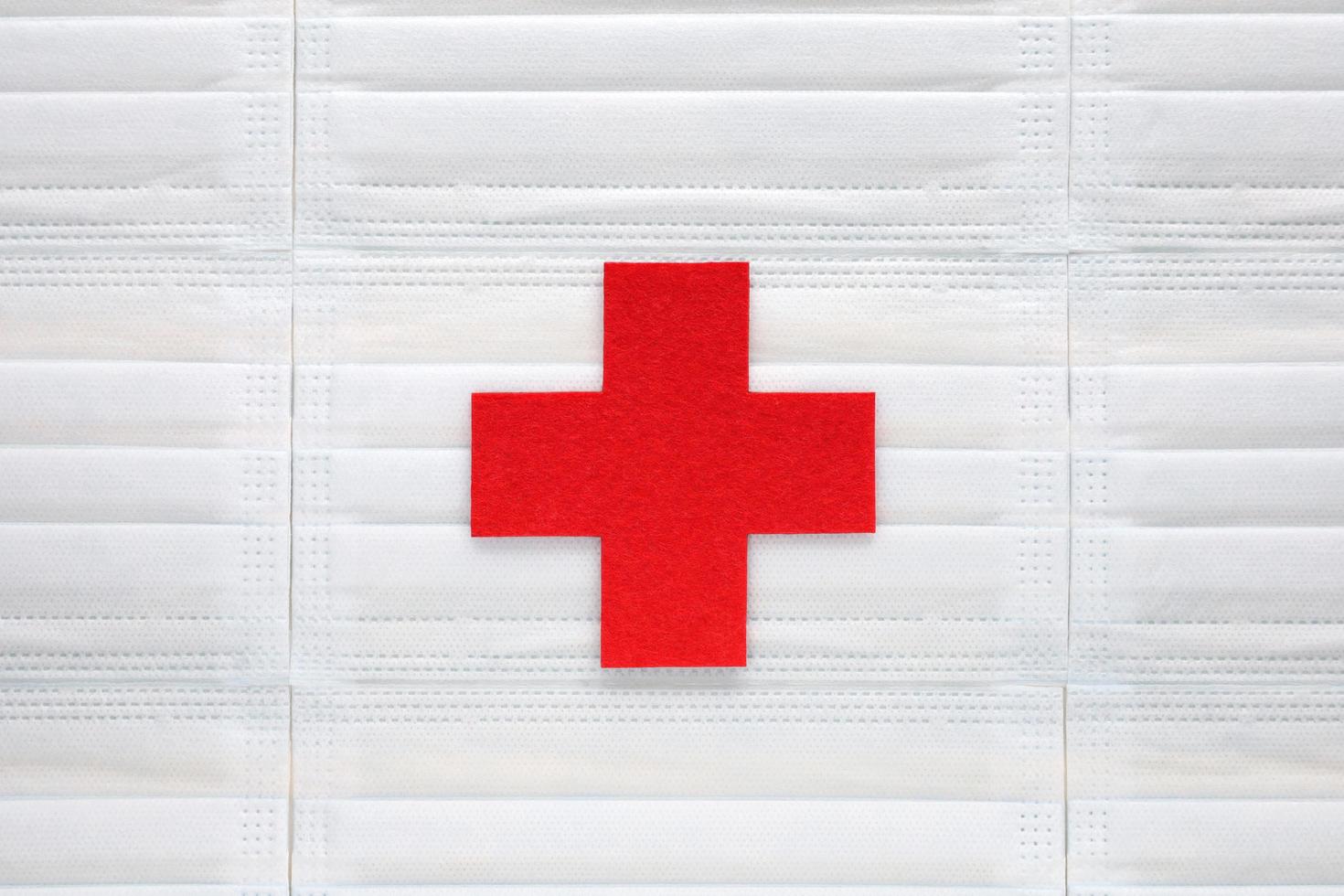 cracovia, polonia, 2021 - símbolo de cruz médica cortado de fieltro rojo centrado en el fondo de máscaras médicas azul claro. sistema de salud, medicina, protección humanitaria, asistencia, ayuda médica. foto