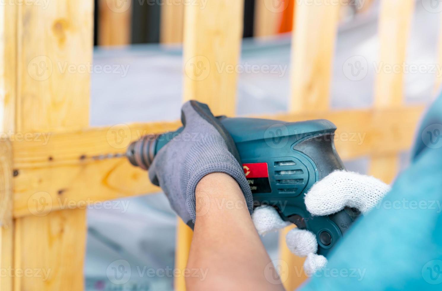 técnico perforando caja de madera con máquina perforadora. montaje de contenedores de maquinaria pesada para su transporte. los carpinteros técnicos usan guantes de seguridad durante el trabajo con taladros eléctricos para perforar tablones. foto