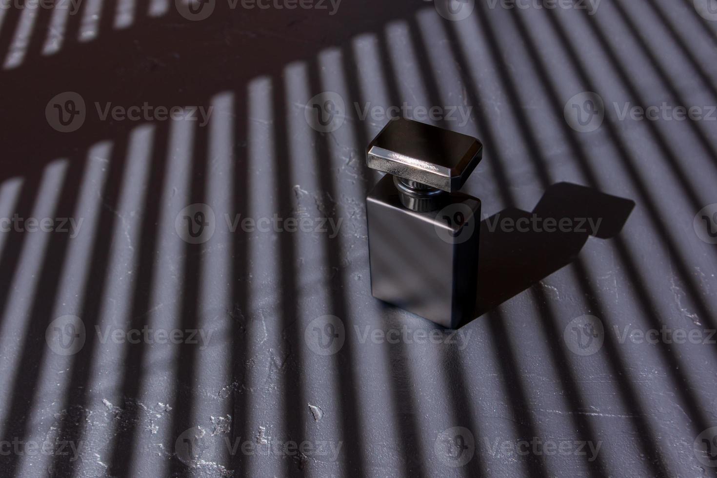 a luxurious black matte bottle of men's perfume water against a background of parallel strips of shadows. advertising concept of men's perfumes. photo
