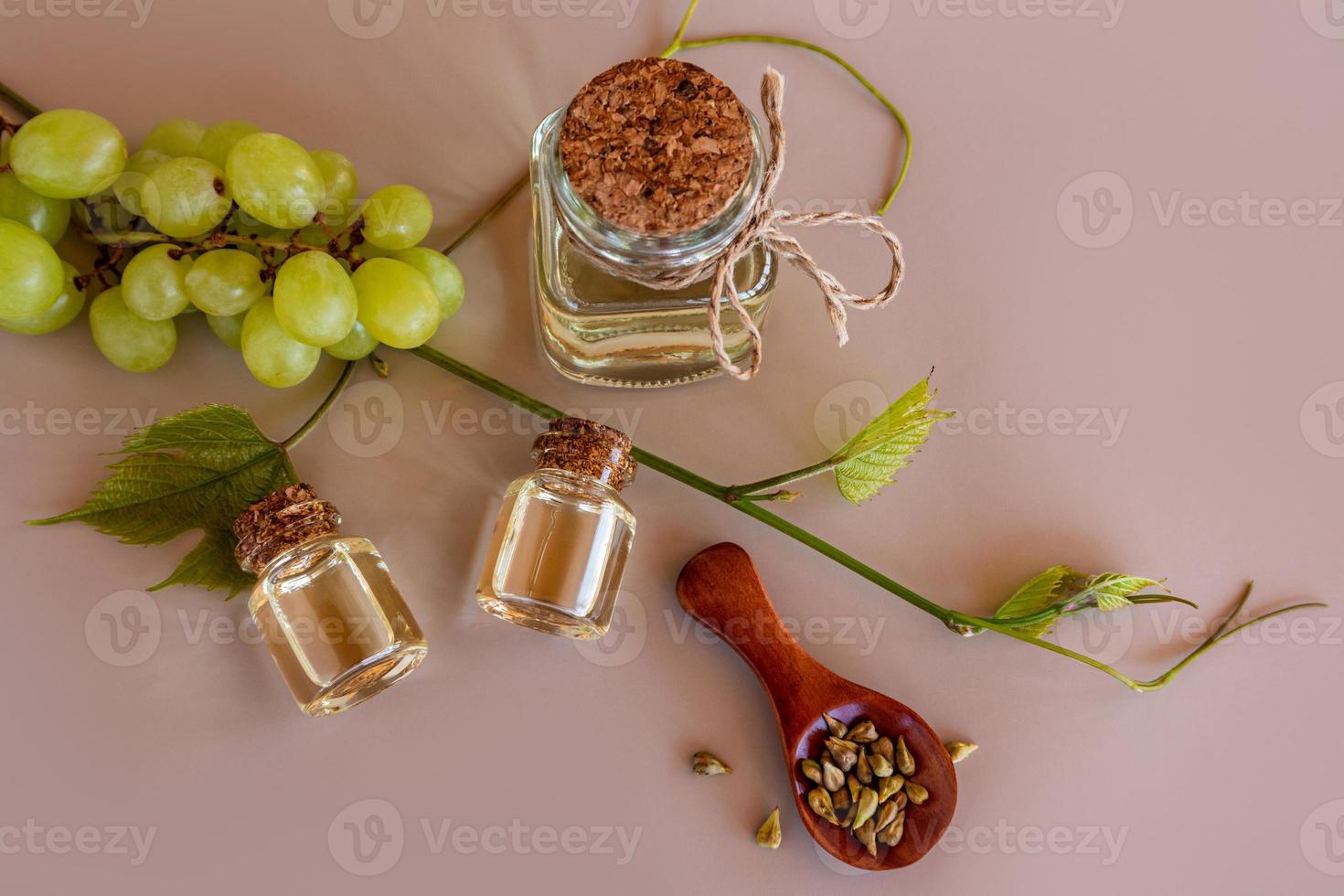 top view of three bottles of natural grape seed oil and a wooden spoon with seeds on a beige background with a vine. photo