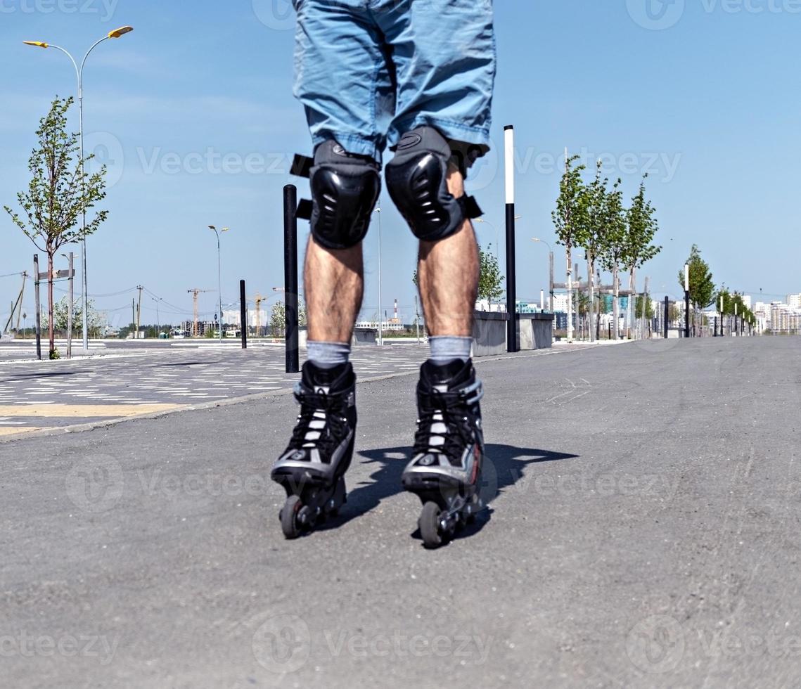 Male legs in roller skates and protective equipment close up riding on the asphalt road in summer, roller blading photo