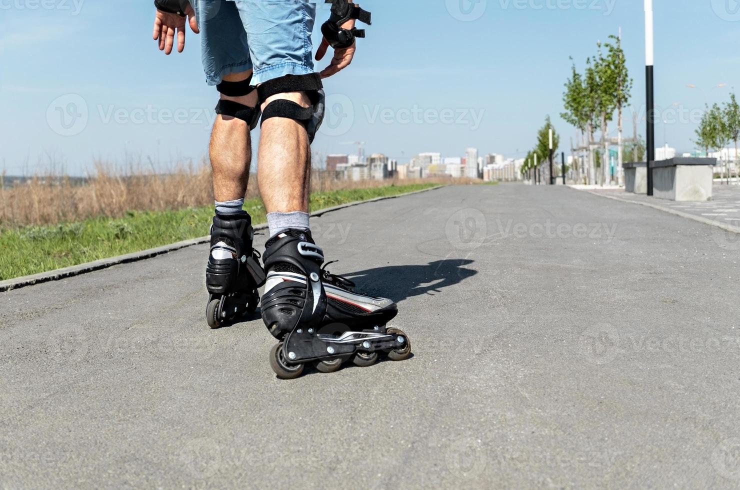 Male legs in roller skates and protective equipment close up riding on the asphalt road in summer photo