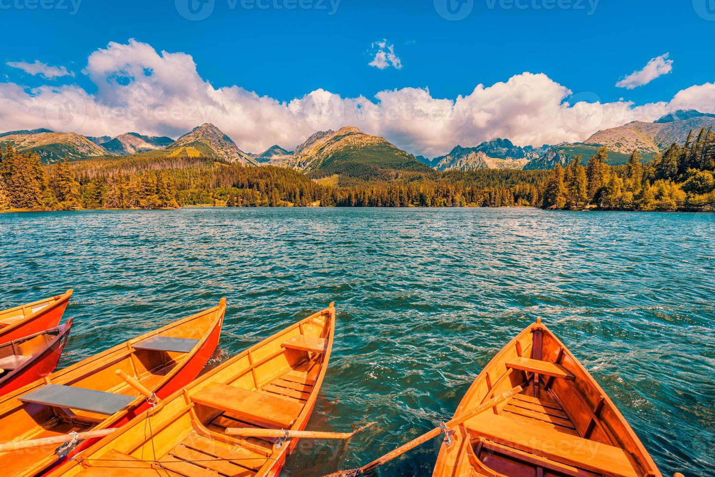 Fantastic mountain lake in National Park High Tatra Europe. Dramatic nature scenic. Beauty world. Wooden boats autumn landscape, beautiful sunny sky clouds relaxing water surface colorful forest trees photo