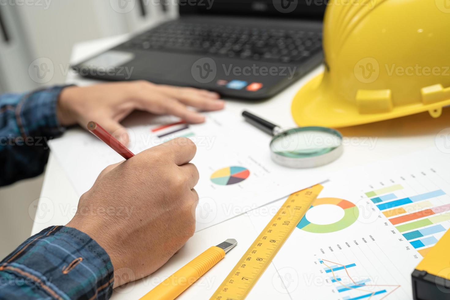 Asian engineer and partner team learn and talk with house plan project blueprint, graph and yellow helmet and engineering construction tools on table work. photo