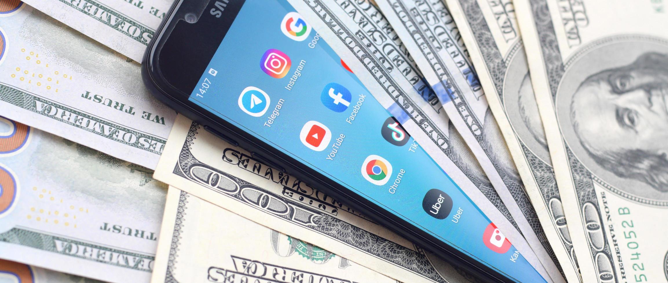 KHARKOV, UKRAINE - MAY 3, 2021 Smartphone screen with many popular apps and lot of hundred dollar bills. Business and social networking concept photo
