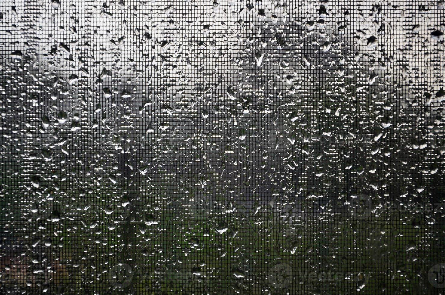 Background image of rain drops on a glass window, which is protected by a mosquito net. Macro photo with shallow depth of field