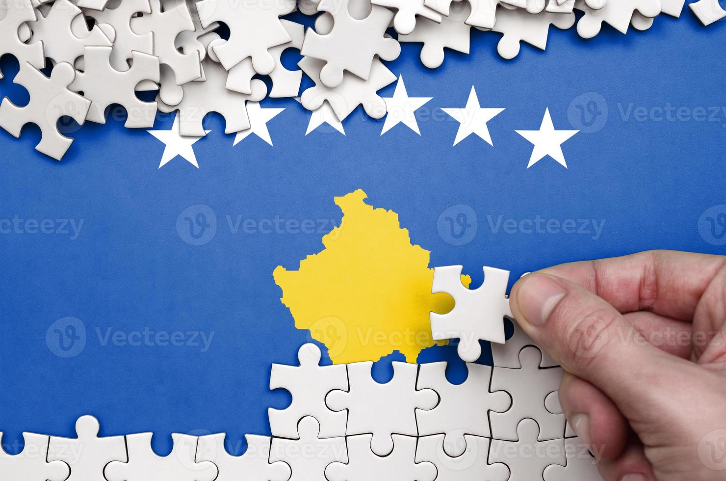 Kosovo flag is depicted on a table on which the human hand folds a puzzle of white color photo