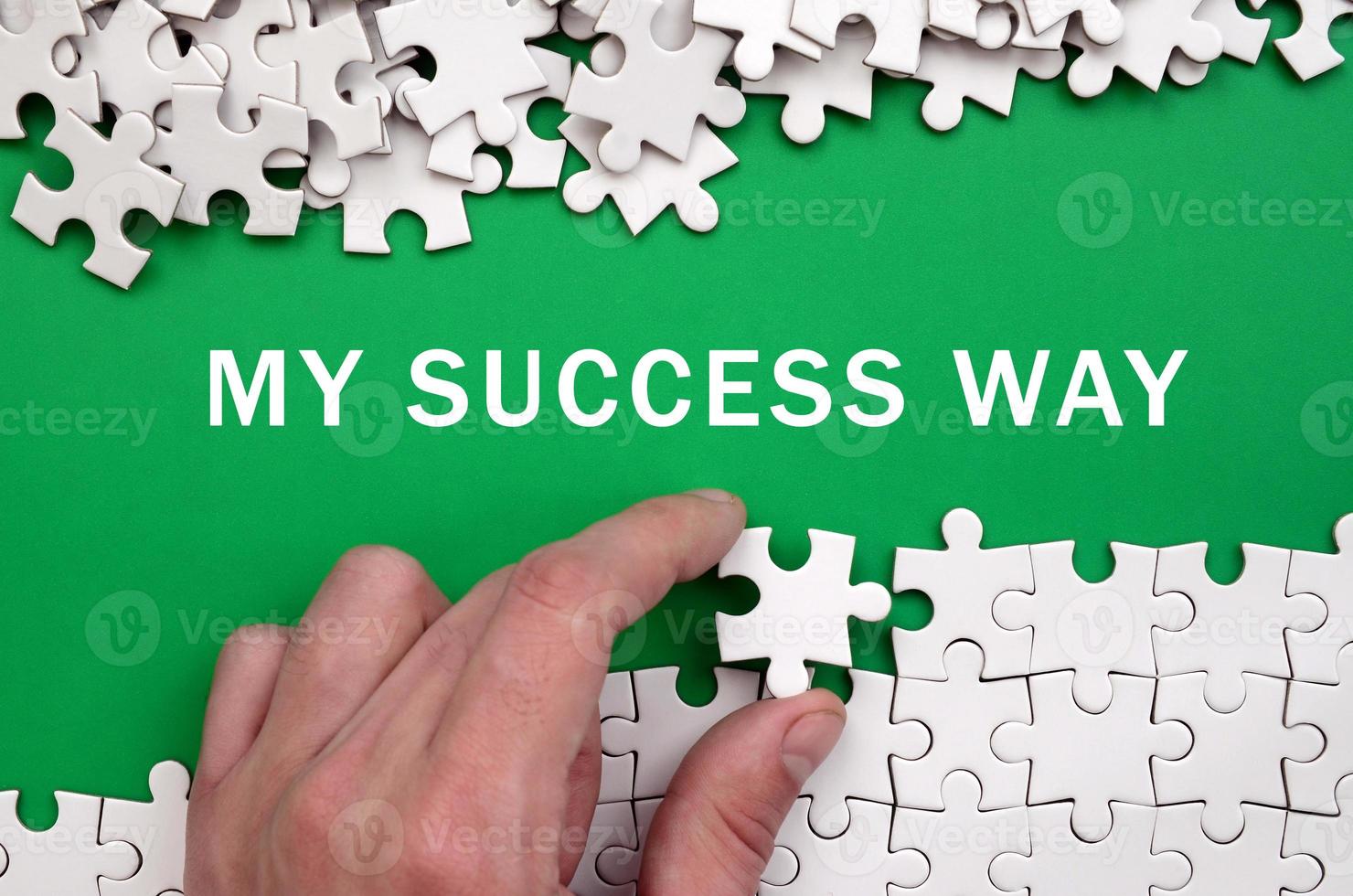 My success way. The hand folds a white jigsaw puzzle and a pile of uncombed puzzle pieces lies against the background of the green surface photo