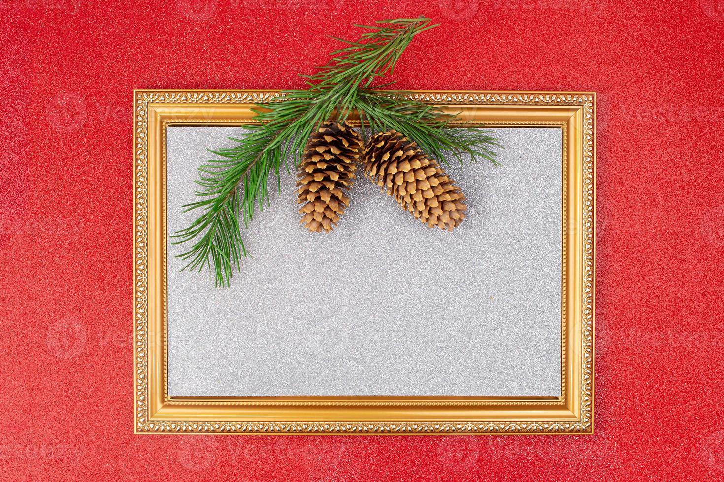 On red shiny background, golden frame with sparkling silver backdrop with spruce branch and cones. Christmas, New Year. Copy space photo