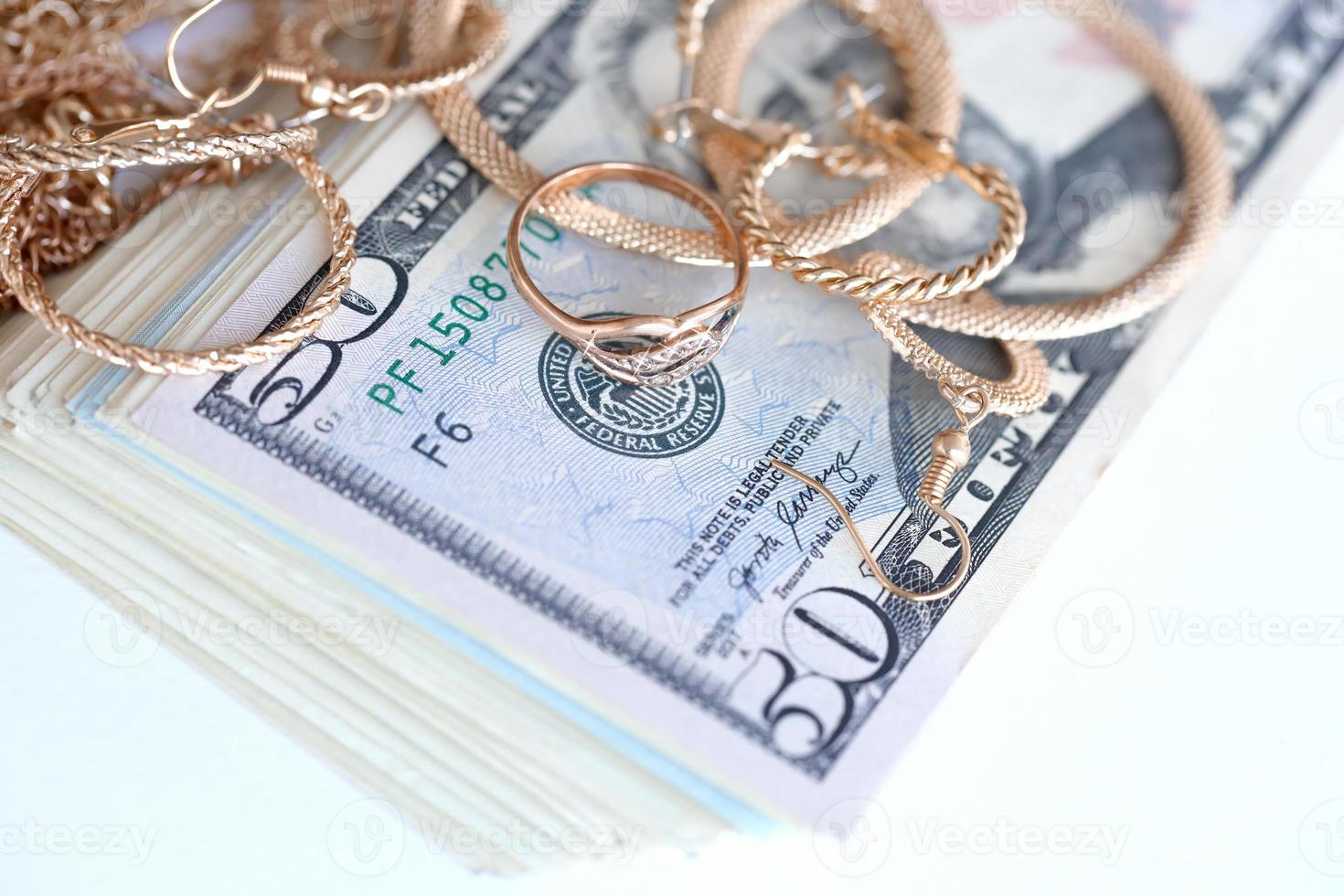 Many expensive golden jewerly rings, earrings and necklaces with big amount of US dollar bills on white background. Pawnshop or jewerly shop photo