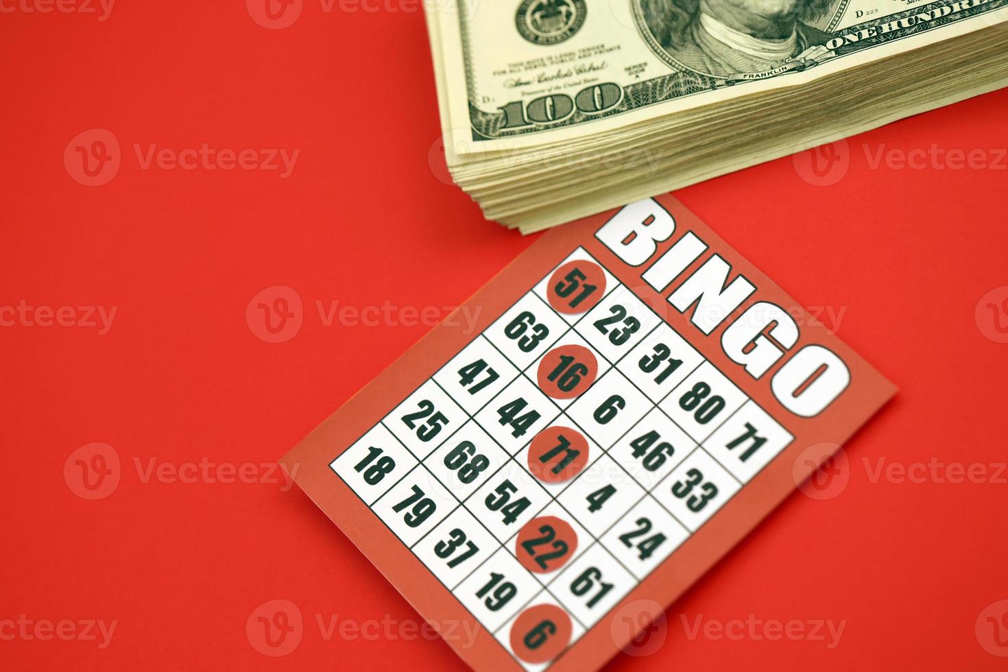 Red bingo board or playing card for winning chips and stack of dollar bills. Classic american or canadian five to five bingo card on red background photo