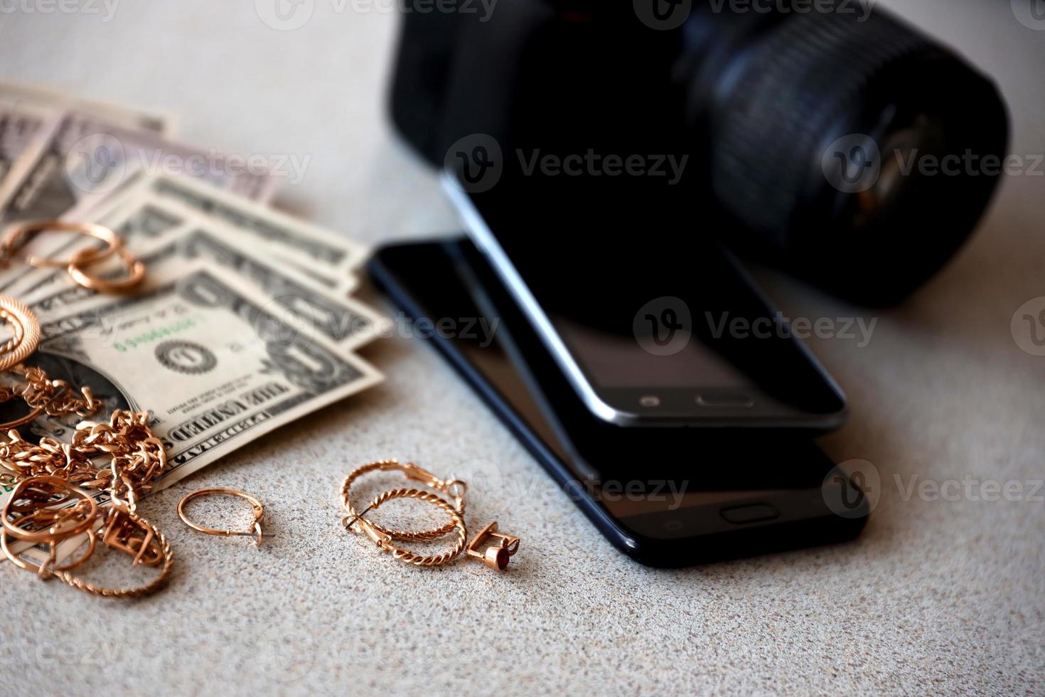 Many expensive golden jewerly rings, earrings and necklaces with big amount of US dollar bills close to smartphones and digital slr camera. Pawn shop photo