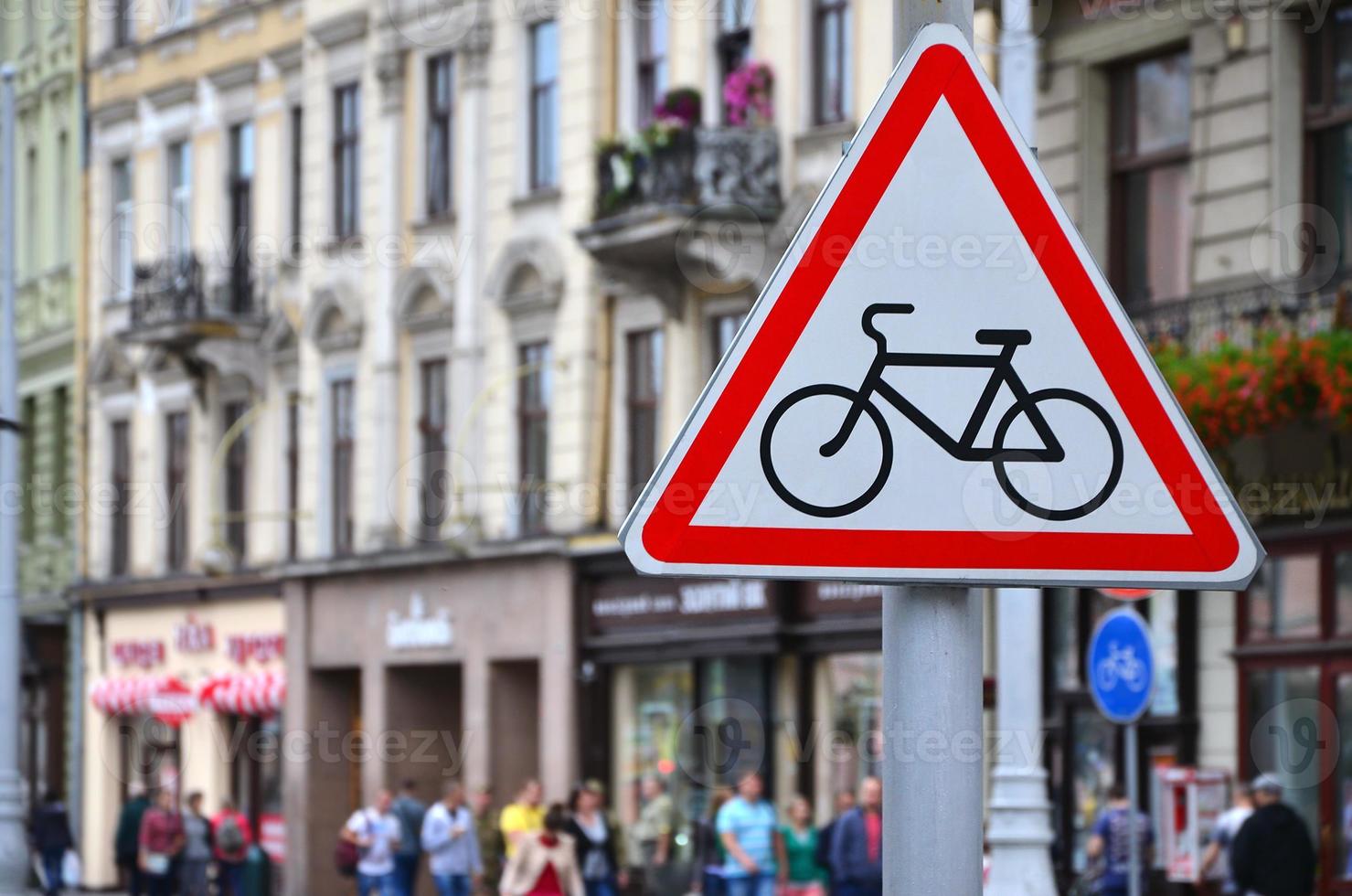 una señal de tráfico con una foto de una bicicleta contra una calle llena de gente. ciclismo permitido