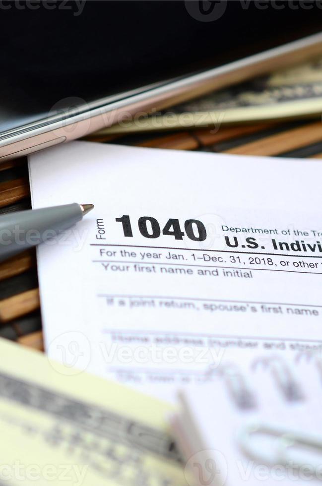 el bolígrafo, el cuaderno, el teléfono inteligente y los billetes en dólares se encuentran en el formulario de impuestos 1040 de la declaración de impuestos sobre la renta de las personas físicas. la hora de pagar impuestos foto