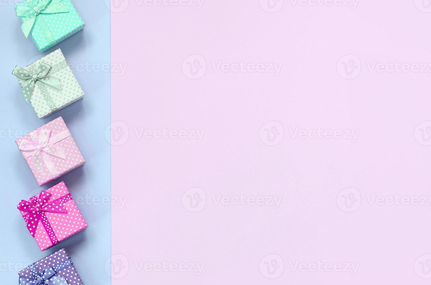 Small gift boxes of different colors with ribbons lies on a violet and pink background photo