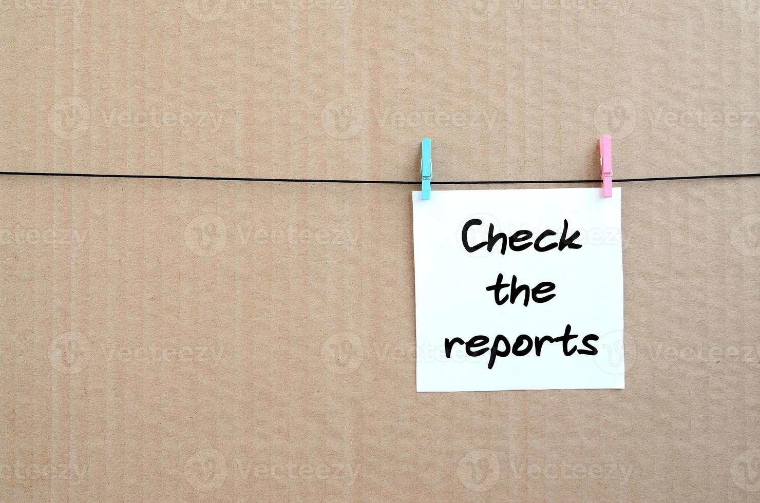 Check the reports. Note is written on a white sticker that hangs with a clothespin on a rope on a background of brown cardboard photo