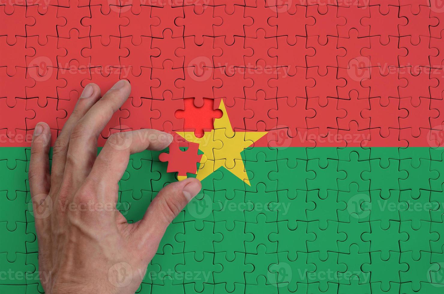 Burkina Faso flag is depicted on a puzzle, which the man's hand completes to fold photo