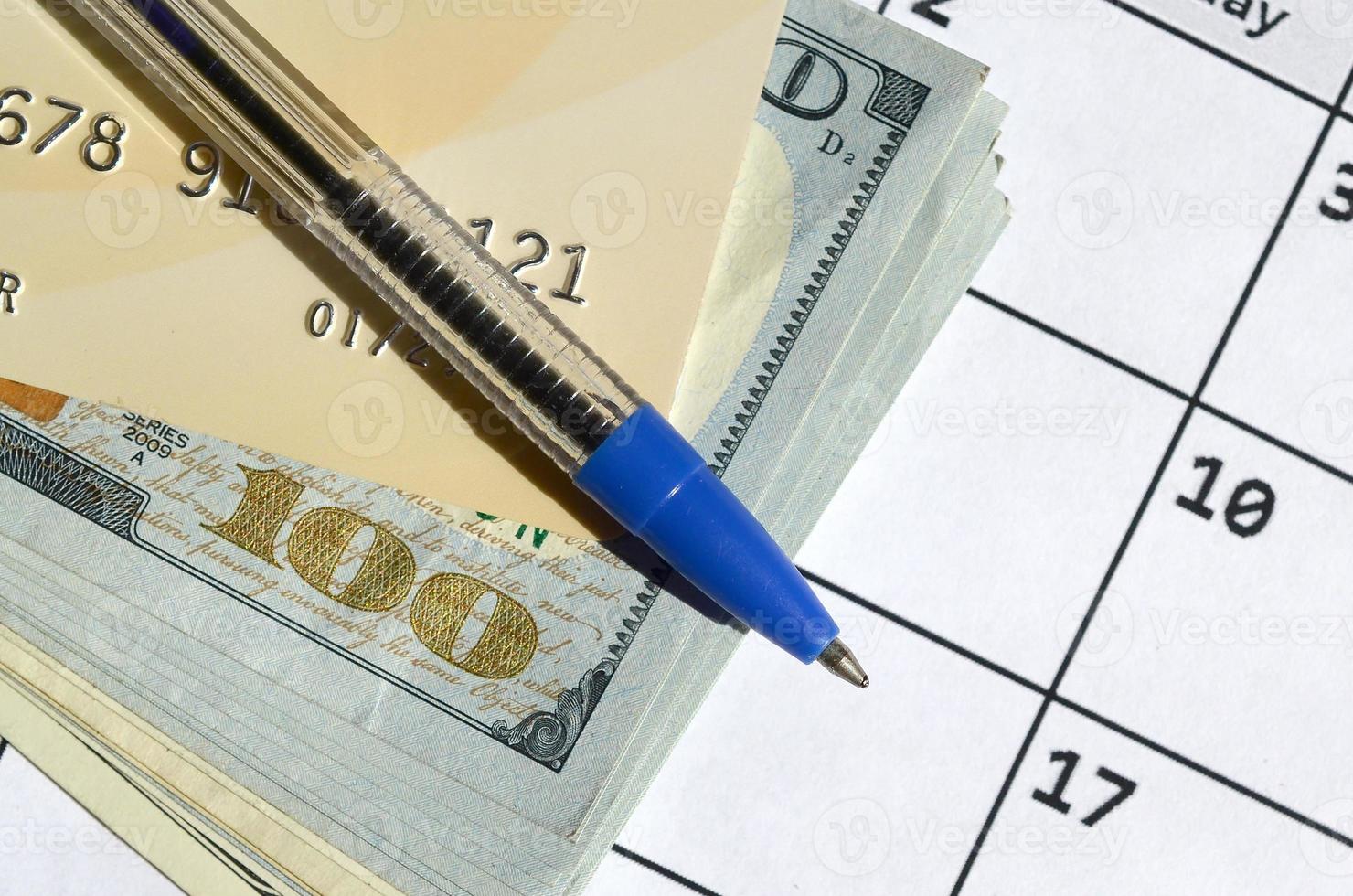 Pen and credit card on many hundred US dollar bills on calendar page close up photo