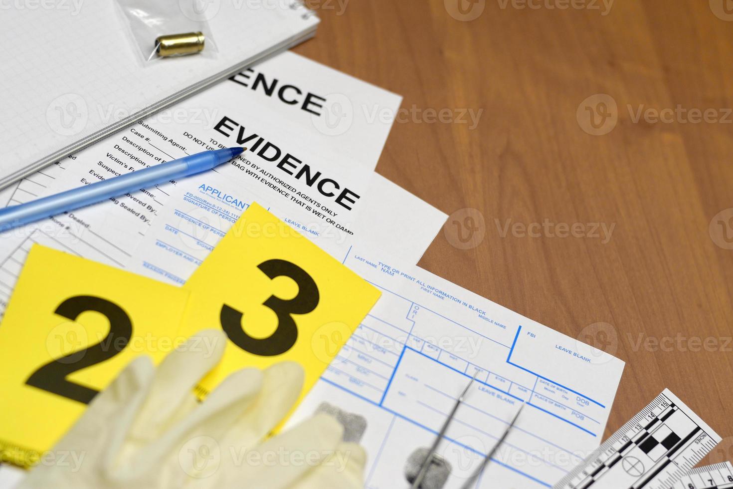 papeleo durante el proceso de investigación de la escena del crimen en el laboratorio csi. etiquetas de evidencia con el solicitante de huellas dactilares y guantes de goma en la mesa de vooden foto