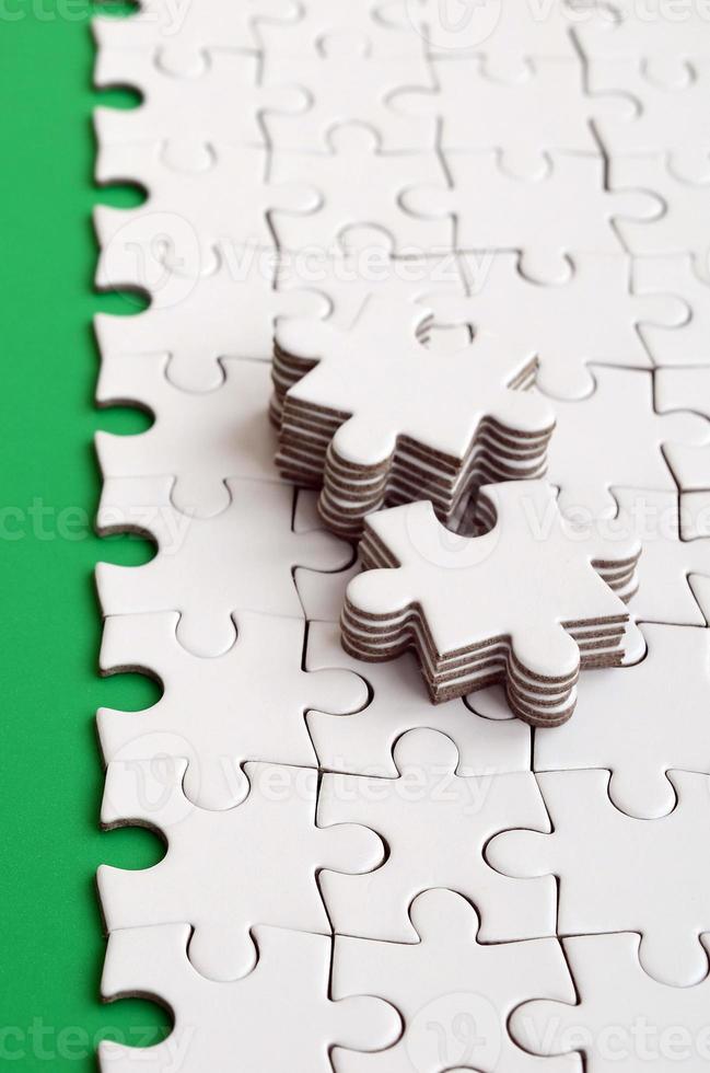 The green path is laid on the platform of a white folded jigsaw puzzle. The missing elements of the puzzle are stacked nearby. Texture image with space for text photo