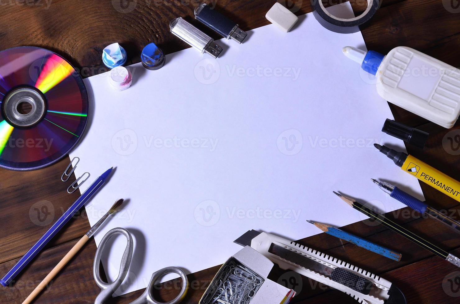 un bodegón de escuela u oficina con una hoja de papel en blanco y muchos suministros de oficina. los útiles escolares se encuentran sobre un fondo de madera marrón. lugar para texto foto