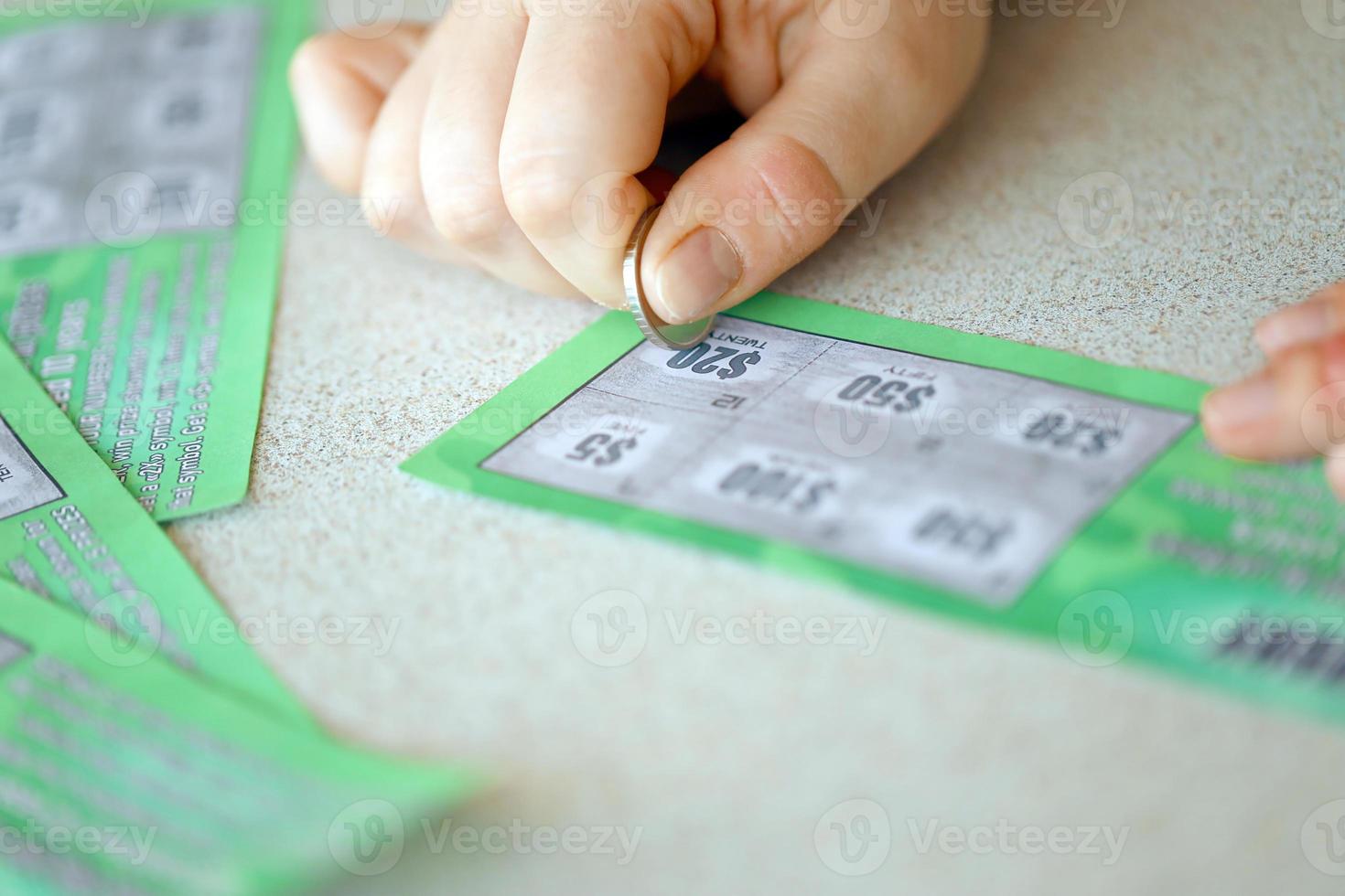 Close up view of silver coin in hand of gambler scratching fake lottery card. Lottery gambling concept, scratching cards lottery photo