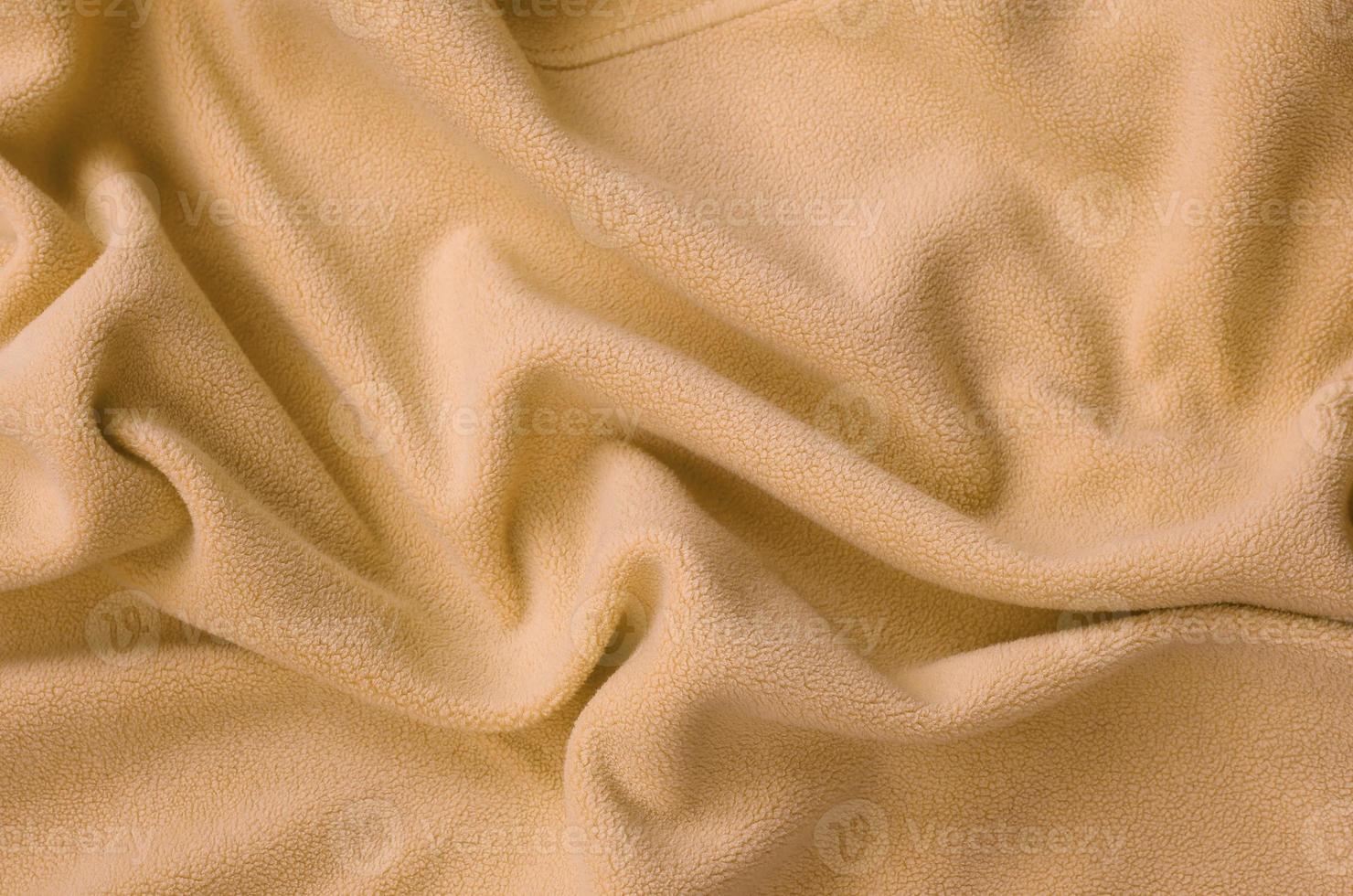 The blanket of furry orange fleece fabric. A background of light orange soft plush fleece material with a lot of relief folds photo
