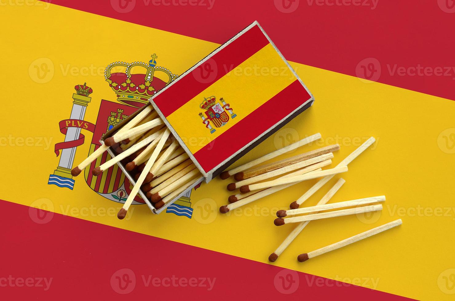 Spain flag is shown on an open matchbox, from which several matches fall and lies on a large flag photo