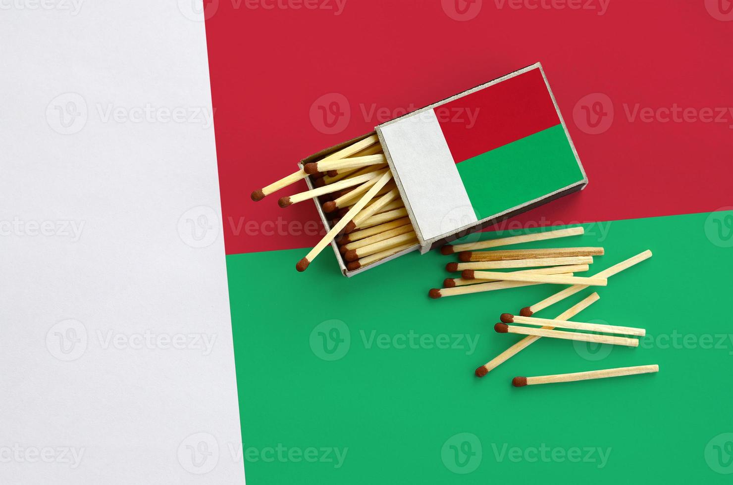 Madagascar flag is shown on an open matchbox, from which several matches fall and lies on a large flag photo