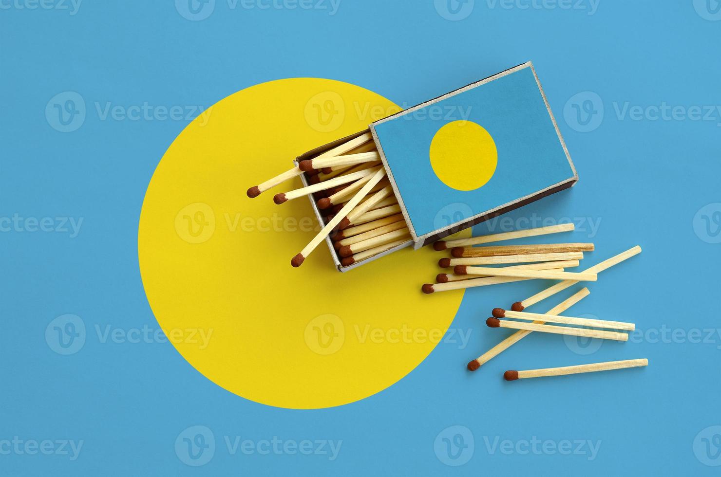 Palau flag is shown on an open matchbox, from which several matches fall and lies on a large flag photo