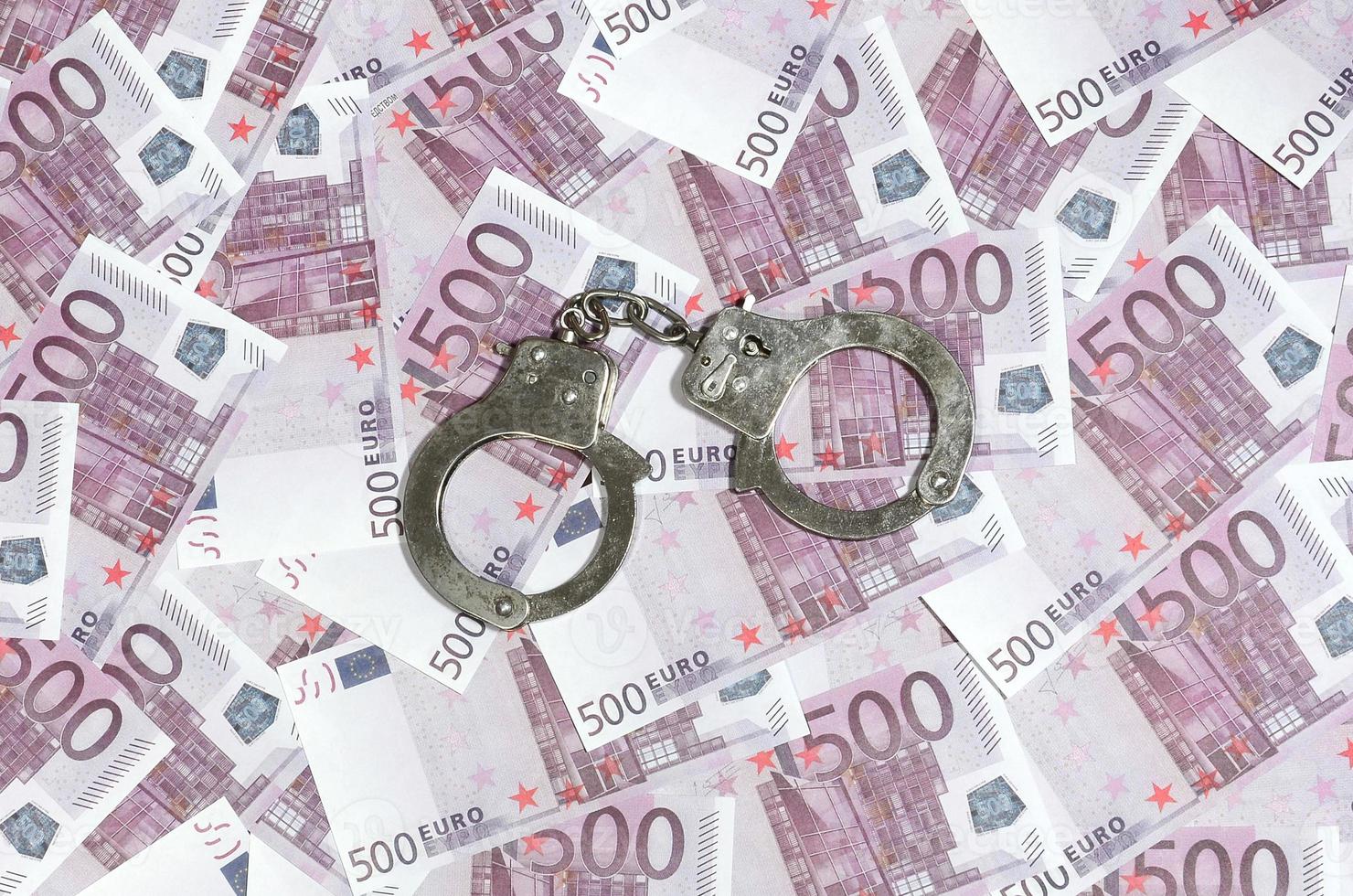 Handcuffs on five hundred euros background. Financial crime, dirty money and corruption concept - 500 money bills and dirty steel handcuffs photo