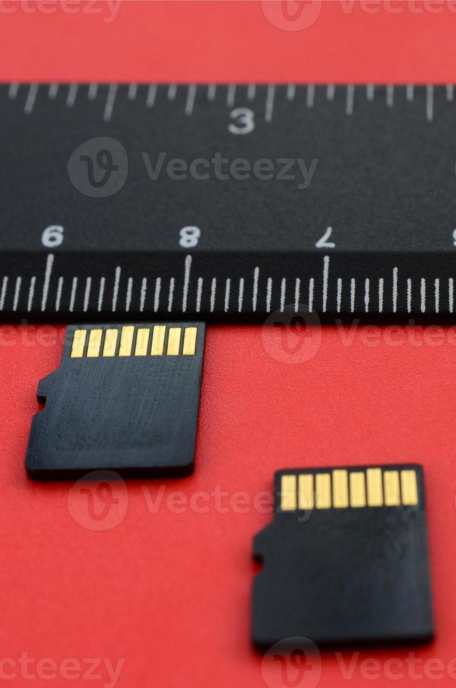 Two small micro SD memory cards lie on a red background next to a black ruler. A small and compact data and information store photo