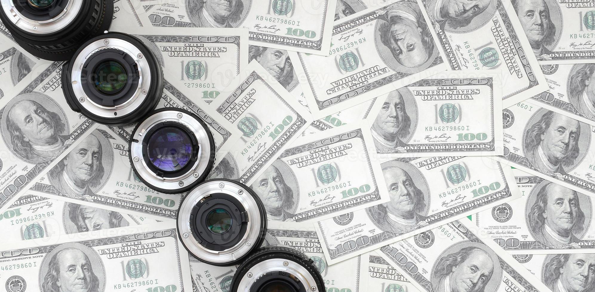 A few photographic lenses lies on the background of a lot of dollar bills. Space for text photo