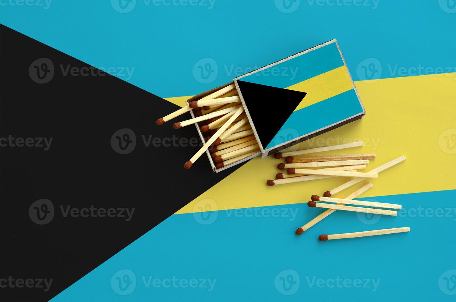 Bahamas flag is shown on an open matchbox, from which several matches fall and lies on a large flag photo